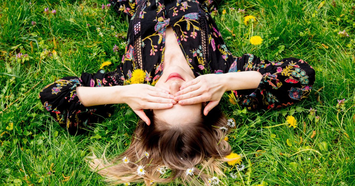 Young woman lying down on green dandelion meadow. Spring time season