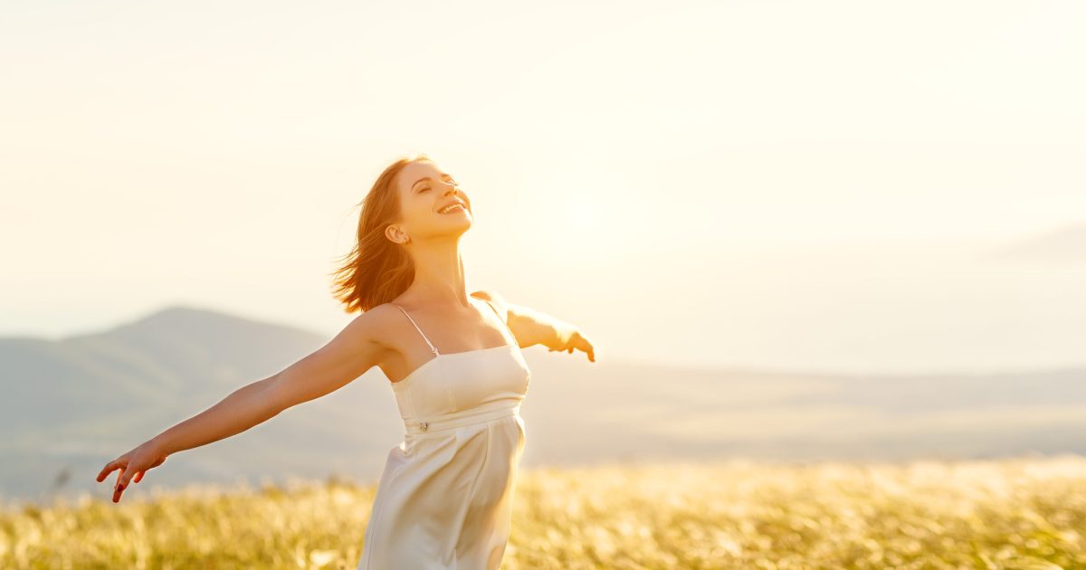 Happy woman standing with her back on the sunset in nature in summer with open hands