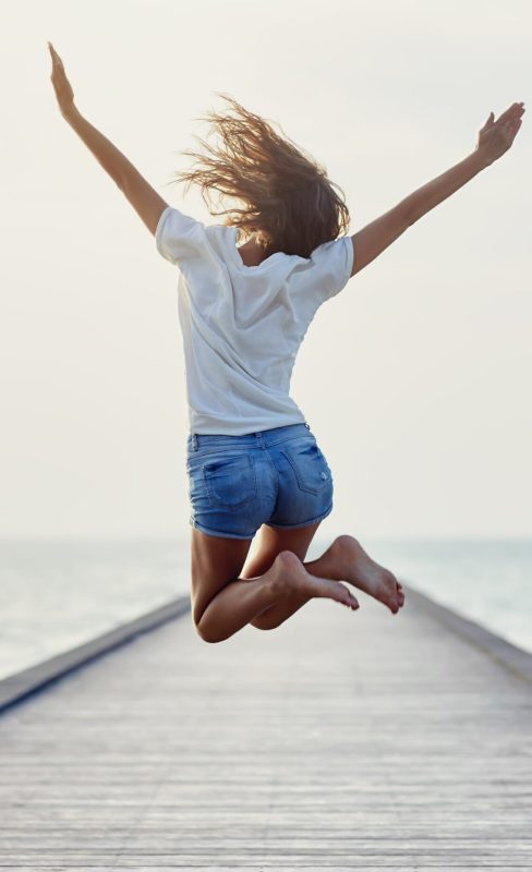 Back view of jumping girl on the pier. Freedom concept