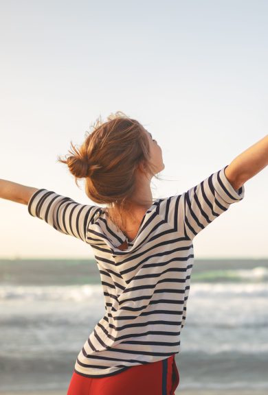 happy young woman enjoying freedom with open hands on sea