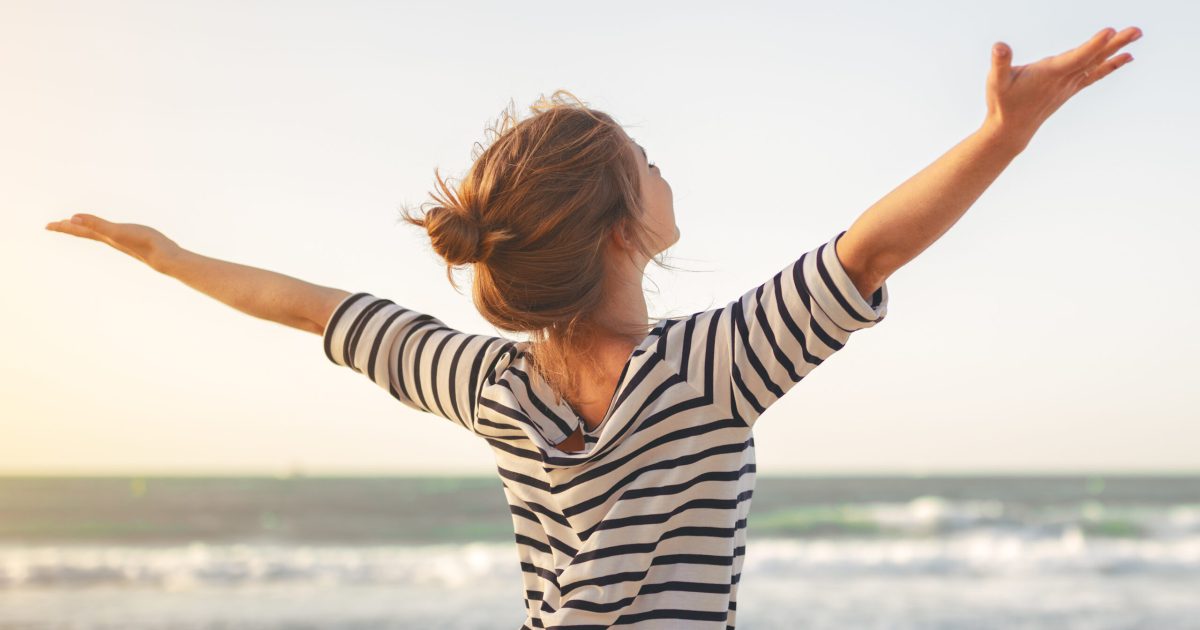 happy young woman enjoying freedom with open hands on sea